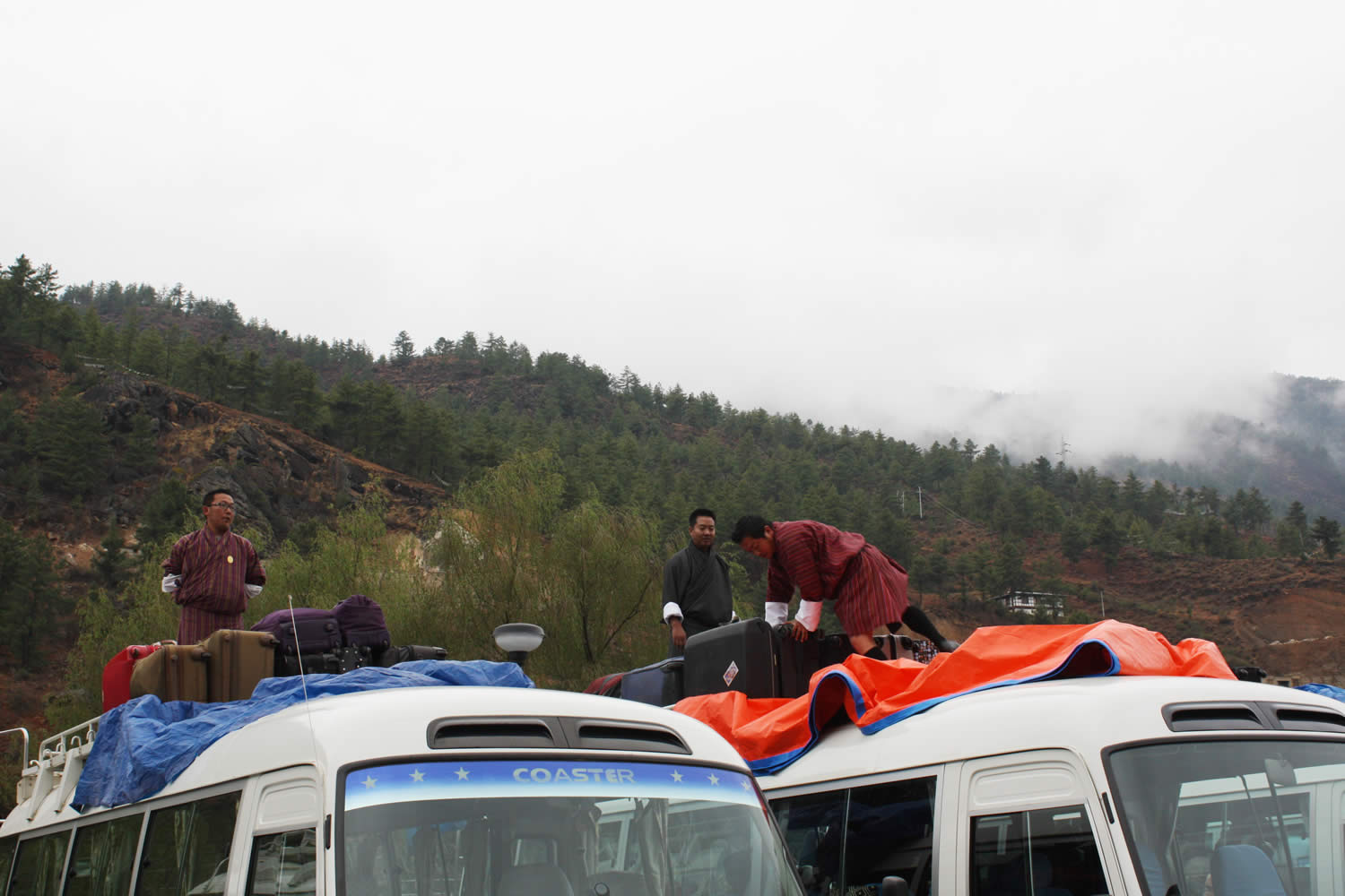 Bhutanese guides and bus drivers pack luggage atop two of the ten buses for the drive to Thimphu.